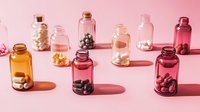 Small glass bottles with pills and supplements arranged in row casting shadows on pink background, minimalist pharmaceutical composition in warm tones.