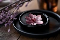Pink lotus flower floating in black ceramic bowl with lavender sprigs on wooden surface, creating zen spa atmosphere for wellness and meditation practices.