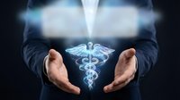 Businessman in dark suit holding glowing medical caduceus symbol between hands, representing healthcare, medicine, and wellness services for medical professionals and industry.