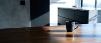 Dark ceramic mug on wooden table in modern minimalist kitchen with natural light, suitable for beverage, lifestyle and interior design projects.