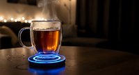 Steaming hot tea in glass mug on glowing blue coaster creates cozy evening atmosphere with warm bokeh lights in background for relaxation concepts.
