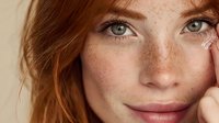 Young redhead woman with freckles and green eyes in natural light portrait showing authentic beauty and confidence for skincare and wellness campaigns.