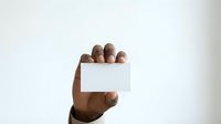 Hand holding blank white business card or empty paper against neutral background, suitable for corporate branding, marketing materials, and professional presentations.