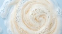 Creamy white foam swirl with bubbles in water creating spiral pattern for skincare cosmetics and beauty product backgrounds.