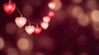 Heart-shaped string lights glowing warmly against blurred burgundy background creating romantic atmosphere for Valentine's Day celebrations and love themes.