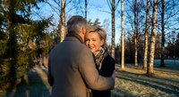Mature couple embracing outdoors in winter park during golden hour sunset, showing love and connection in natural forest setting with bare trees.