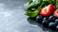 Fresh ripe strawberries and blueberries with green spinach leaves on dark stone background, selective focus with copy space for healthy eating.