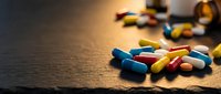 Colorful pharmaceutical capsules and pills scattered on wooden surface with warm lighting for medical and healthcare concepts.