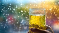 Golden beer in glass with condensation droplets, held against colorful bokeh background with warm and cool light effects. Perfect for beverage, refreshment, and celebration themes.