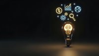 Glowing light bulb with business icons floating above on dark background representing innovation, creativity and entrepreneurial success in corporate strategy.