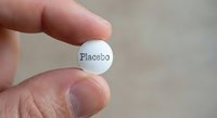 Hand holding white pill tablet labeled placebo for medical research clinical trial pharmaceutical testing concept.