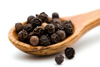 Black peppercorns in wooden spoon on white background, aromatic whole dried spice berries, macro food photography for cooking and seasoning concepts.