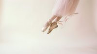 Ballerina feet in pointe shoes with pink ribbons, soft tutu visible, elegant dance pose on light pastel background, grace and art.