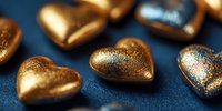 Golden heart-shaped chocolates with metallic shimmer on dark blue background, luxury confectionery for romantic occasions and gift giving.