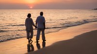 Romantic couple holding hands walking on beach at sunset with golden ocean waves and warm sky colors creating peaceful moment for love and togetherness.