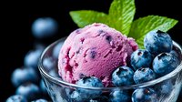 Vibrant blueberry ice cream scoop in glass bowl garnished with fresh berries and mint leaves on dark background, macro food photography for dessert menu.