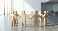Wooden human figures holding hands in circle on office floor representing teamwork, unity, collaboration and business partnership concepts.