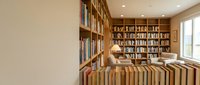 Cozy home library with wooden bookshelves filled with books, comfortable reading chair and warm lighting creating perfect study atmosphere for book lovers.