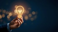 Businessman hand holding glowing light bulb against dark background with bokeh lights representing innovation, creativity and bright ideas for business solutions.
