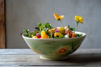Fresh summer salad with edible flowers, berries and mixed greens served in vintage ceramic bowl on rustic wooden table against gray wall background.