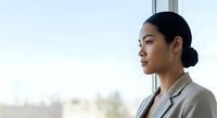 Young Asian woman in business attire gazing thoughtfully out window, professional contemplation and career aspirations concept for corporate and leadership themes.