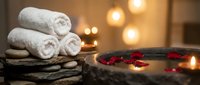 Spa wellness setup with rolled white towels, rose petals and candles creating relaxing atmosphere for massage therapy and self-care rituals.