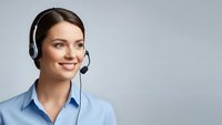 Smiling young Caucasian woman customer service representative wearing headset and blue shirt on gray background for business communication concepts.