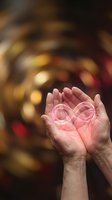 Cupped hands holding glowing pink heart symbol with warm bokeh lights background representing love, care, compassion and emotional wellness concepts.