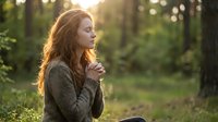 Young redhead woman in cozy sweater enjoying peaceful moment in sunlit forest during golden hour for wellness and mindfulness content.