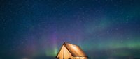 Illuminated camping tent under vibrant aurora borealis with starry night sky creating magical outdoor adventure scene for travel and nature enthusiasts.