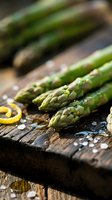 Fresh green asparagus spears with sea salt and lemon zest on rustic wooden cutting board, ready for healthy cooking and gourmet meal preparation.