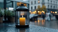 Glowing lantern with burning candle on rainy evening, water drops on surface, blurred urban bokeh lights in background, moody atmospheric cityscape.