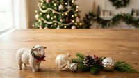 Cute corgi dog with red collar standing on wooden floor next to festive holiday decorations, evergreen branches, pinecones and ornaments, with decorated tree in blurred background for seasonal celebrations.