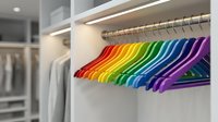 Colorful rainbow hangers arranged in spectrum order on closet rod in modern organized wardrobe with white shelving and LED lighting for home organization.