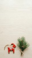 Scandinavian red wooden horse ornament with white folk pattern and fresh evergreen pine sprig tied with twine on light wood surface for holiday decoration and seasonal design projects.
