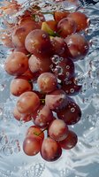 Fresh red grapes splashing into clear water with bubbles surrounding the fruit, creating a refreshing and dynamic food photography scene.
