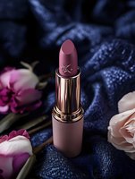 Luxurious rose gold lipstick surrounded by delicate roses and dark blue silk fabric creates romantic mood for beauty and cosmetic advertising.