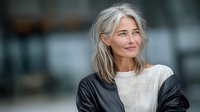 Confident mature businesswoman with silver gray hair smiling in modern office environment. Professional corporate portrait for business and career content.