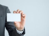Businessman in dark suit holding blank white business card for corporate branding and professional networking purposes.