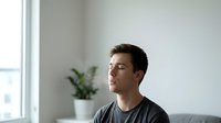 Young Caucasian man with closed eyes practicing mindfulness meditation in bright modern living room with houseplant for wellness and mental health.