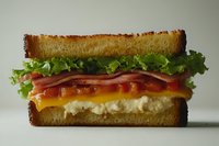 Delicious sandwich with toasted bread, fresh lettuce, ham slices, melted cheese, and tomato sauce, showcasing layers of vibrant ingredients.