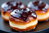 Fresh baked donuts with dark chocolate glaze and cream filling on black plate, extreme close up view showing glossy texture and rich details.