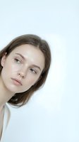 Young Caucasian woman with natural makeup and brown hair wearing white top against clean background for beauty and skincare concepts.