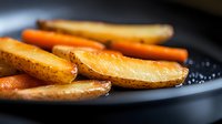 Golden roasted potato wedges with crispy skin and fluffy interior seasoned with herbs and salt in dark pan for cooking and food preparation.