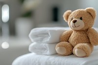 Soft brown teddy bear sitting on folded white towels in bright bathroom setting, creating cozy and welcoming atmosphere for children and spa concepts.