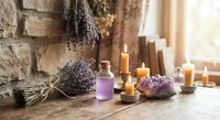 Lavender spa aromatherapy setup with essential oil bottles, dried herbs, burning candles and natural stone creating relaxing wellness atmosphere.