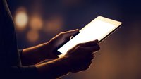 Person holding glowing tablet device in dark environment with warm bokeh lights creating atmospheric digital technology scene for modern communication.