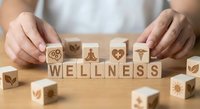 Hands arranging wooden blocks spelling WELLNESS with healthcare symbols on natural wood surface for holistic health and medical wellness concepts.