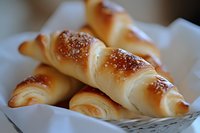 Fresh baked croissants with golden crust and sesame seeds served in white paper, close up view of French pastries for breakfast or bakery menu.