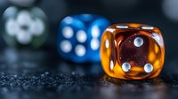 Translucent orange and blue dice on dark textured surface with selective focus creating atmospheric gambling composition. Macro photography highlights crystal clarity.